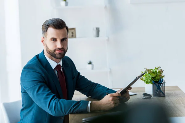 Selective focus of handsome man holding clipboard near table — Stock Photo