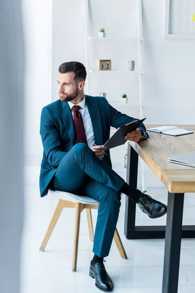 Selective focus of handsome recruiter with crossed legs sitting on chair near table — Stock Photo