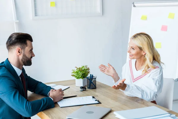 Cheerful and bearded recruiter looking at woman gesturing in office — Stock Photo