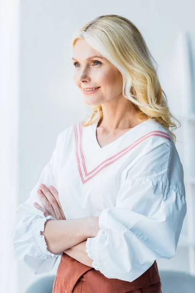 Happy blonde woman standing with crossed arms in office — Stock Photo