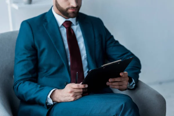 Vista recortada del hombre barbudo sentado en sillón con portapapeles — Stock Photo