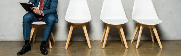 Plan panoramique de l'homme assis sur une chaise blanche et tenant presse-papiers — Photo de stock