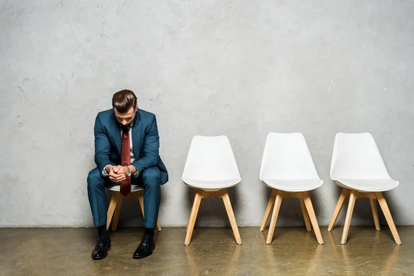 Homem bonito sentado com as mãos apertadas na cadeira branca enquanto espera trabalho interviw — Fotografia de Stock