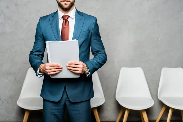 Cropped view of bearded man holding folder while standing near white chairs — Stock Photo