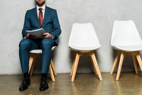 Vista recortada hombre barbudo sentado en silla blanca y carpeta de celebración — Stock Photo