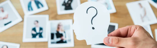 Panoramic shot of man holding paper with human head and question mark near photos — Stock Photo