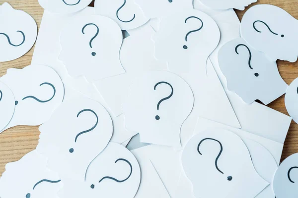 Question marks on paper with human heads on wooden table — Stock Photo