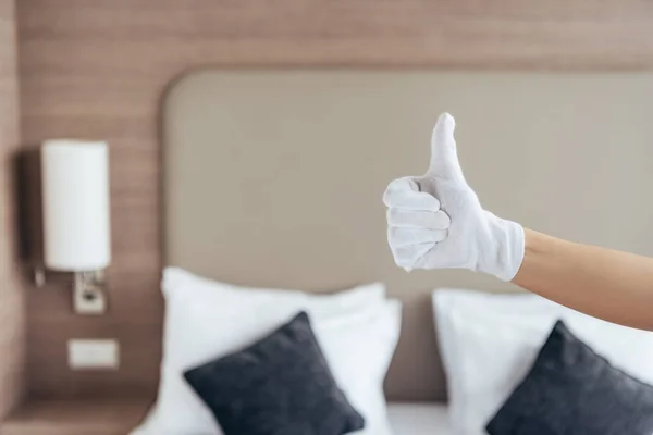 Vista parcial de la criada en guante blanco mostrando el pulgar hacia arriba en la habitación del hotel — Stock Photo