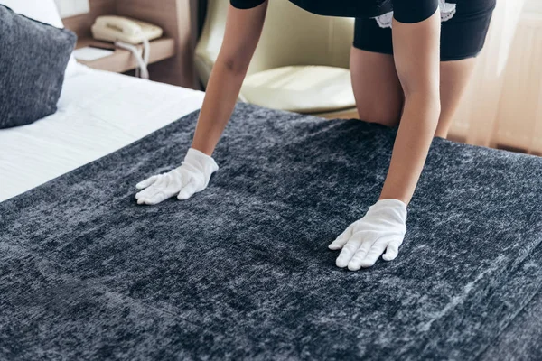 Cropped view of maid in white gloves cleaning bed in hotel room — Stock Photo