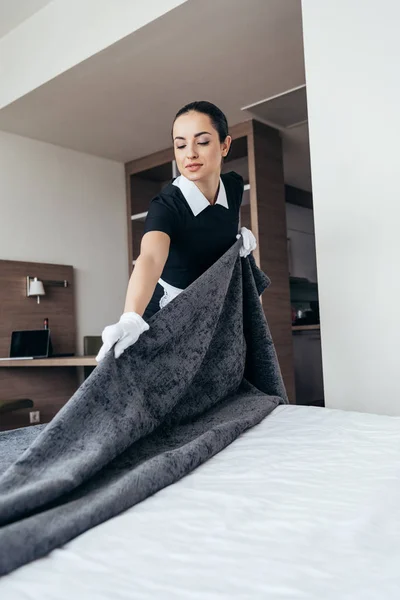 Hübsche Hausmädchen in weißen Handschuhen putzen Bett im Hotelzimmer — Stockfoto