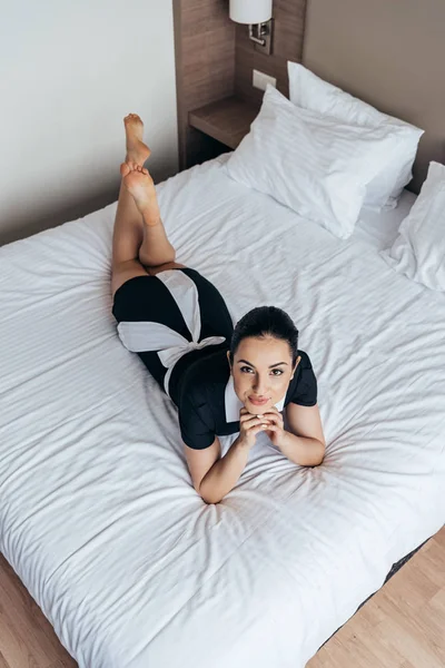 Вид сверху на улыбающуюся босиком горничную лежащую на кровати в номере отеля — стоковое фото