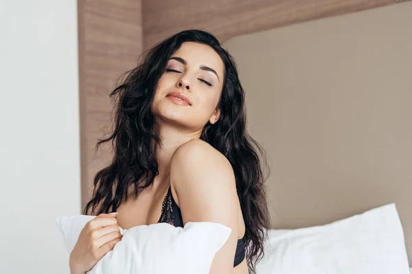 Sexy mujer joven en lencería sosteniendo almohada blanca en el dormitorio - foto de stock