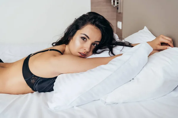 Sensual brunette young woman in black bra lying on pillow — Stock Photo