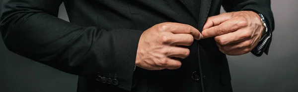 Cropped view of african american businessman in suit fixing button on dark background, panoramic shot — Stock Photo