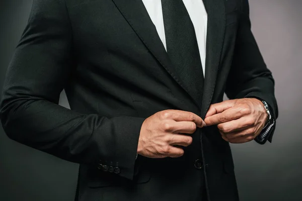 Cropped view of african american businessman in suit fixing button on dark background — Stock Photo