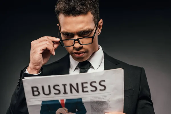 Empresário afro-americano em óculos e terno ler jornal de negócios em fundo escuro — Fotografia de Stock