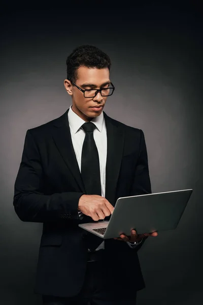 Hombre de negocios afroamericano utilizando el ordenador portátil sobre fondo oscuro - foto de stock