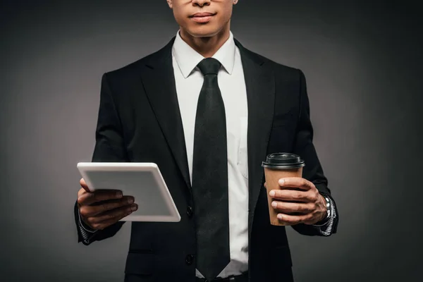 Частичный взгляд на африканского американского бизнесмена, держащего кофе, чтобы пойти и цифровой планшет на темном фоне — стоковое фото