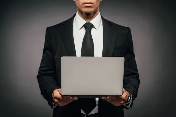 Partial view of african american businessman holding laptop on dark background — Stock Photo