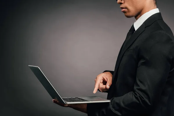 Teilansicht eines afrikanisch-amerikanischen Geschäftsmannes mit Laptop auf dunklem Hintergrund — Stockfoto
