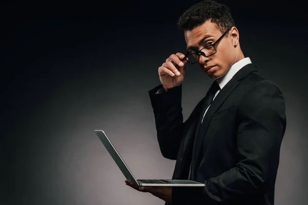 African american businessman holding laptop and looking at camera on dark background — Stock Photo