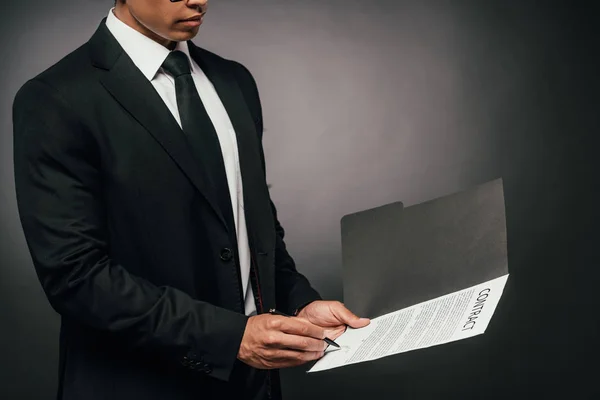 Cropped view of african american businessman signing contract on dark background — Stock Photo