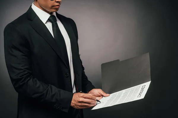 Vista recortada del empresario afroamericano firmando contrato sobre fondo oscuro - foto de stock