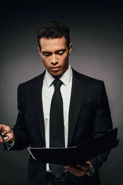 African american businessman reading documents in folder on dark background — Stock Photo