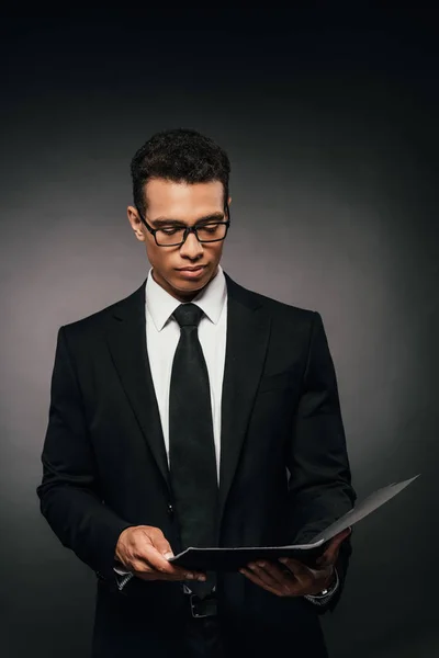 Hombre de negocios afroamericano leyendo contrato sobre fondo oscuro - foto de stock