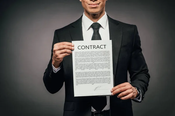 Partial view of cheerful african american businessman showing contract on dark background — Stock Photo