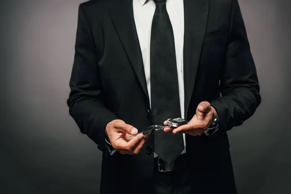Vista recortada del hombre de negocios afroamericano sosteniendo las llaves del coche sobre fondo oscuro - foto de stock