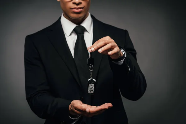 Vista parcial del hombre de negocios afroamericano mostrando las llaves del coche sobre fondo oscuro - foto de stock