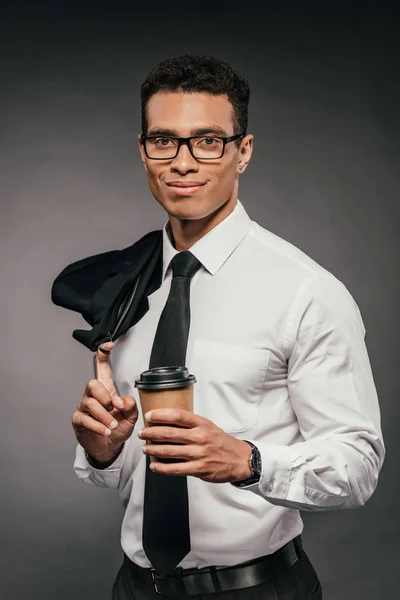 Sorridente Africano americano empresário segurando blazer, copo de papel no fundo escuro — Fotografia de Stock
