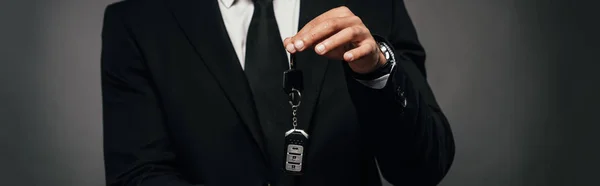 Cropped view of african american businessman showing car keys on dark background, panoramic shot — Stock Photo