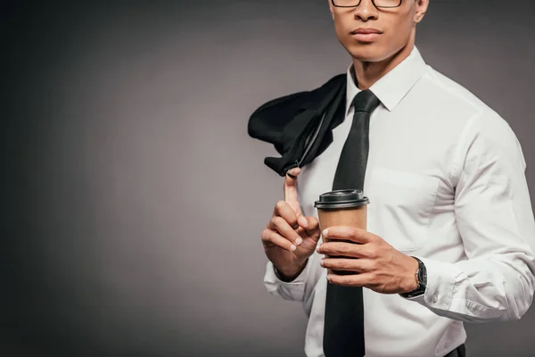 Cropped view of african american businessman holding blazer and coffee to go on dark background — Stock Photo