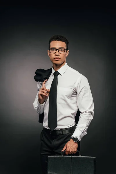 Africano americano empresário segurando blazer e pasta de couro no fundo escuro — Fotografia de Stock