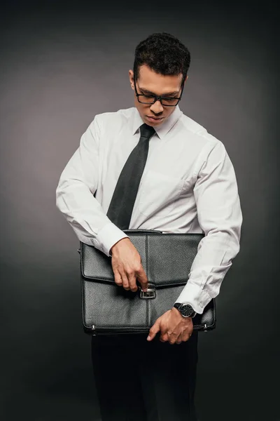 Hombre de negocios afroamericano cerrando maleta de cuero sobre fondo oscuro - foto de stock