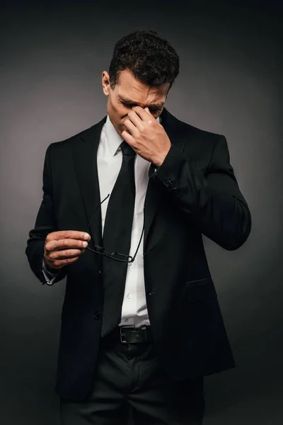 Cansado afroamericano hombre de negocios en traje frotando sus ojos sobre fondo oscuro - foto de stock