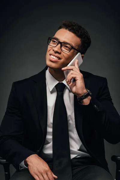 Улыбающийся африканский американский бизнесмен разговаривает по смартфону на тёмном фоне — стоковое фото
