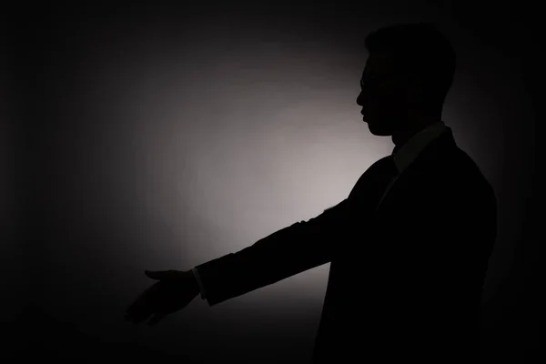 Vista lateral de silueta negra del hombre de negocios haciendo gesto de saludo con luz de fondo - foto de stock
