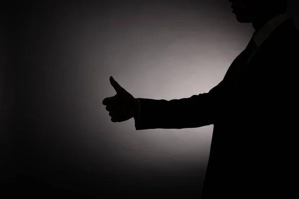 Vista recortada de silueta negra del hombre de negocios mostrando el pulgar hacia arriba con luz de fondo - foto de stock