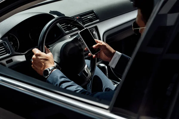 African american businessman in suit and sunglasses driving car and using smartphone at sunny day — Stock Photo