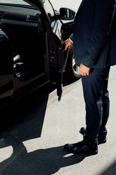 Partial view of african american businessman in suit opening car door at sunny day — Stock Photo