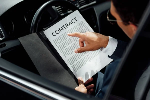 Обрізаний вид афроамериканського бізнесмена в костюмі, який читає контракт в машині в сонячний день — стокове фото