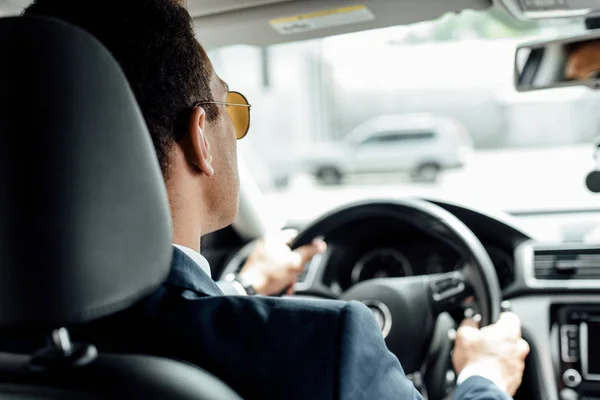 Vista trasera del hombre de negocios afroamericano en traje y gafas de sol que conducen el coche - foto de stock