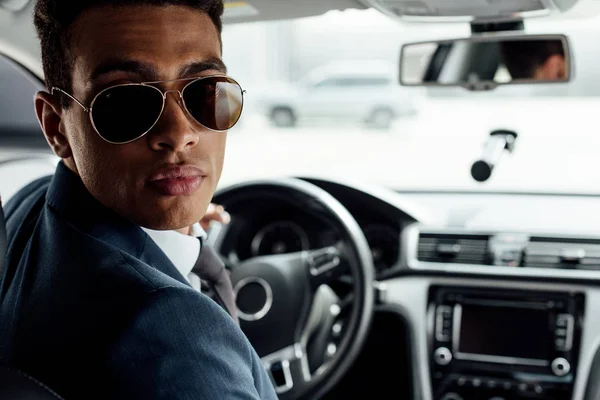 Homme d'affaires afro-américain en costume et lunettes de soleil voiture de conduite — Photo de stock