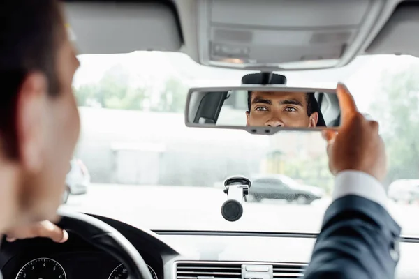 Hombre de negocios afroamericano en traje coche de conducción y mirando el espejo - foto de stock