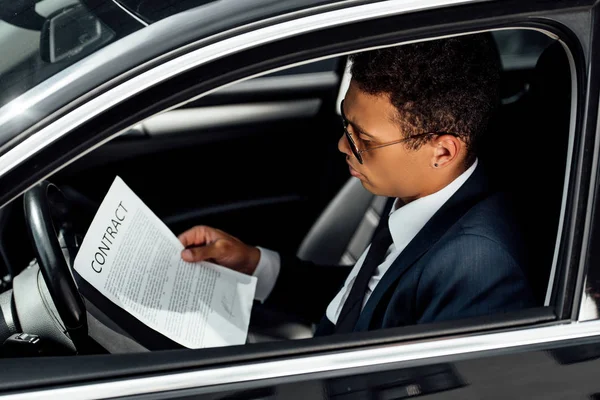 Hombre de negocios afroamericano en traje contrato de lectura en coche - foto de stock