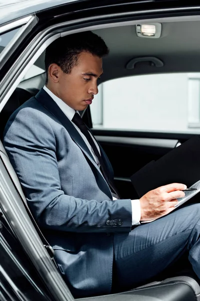 Side view of african american businessman in suit reading contract in car — Stock Photo