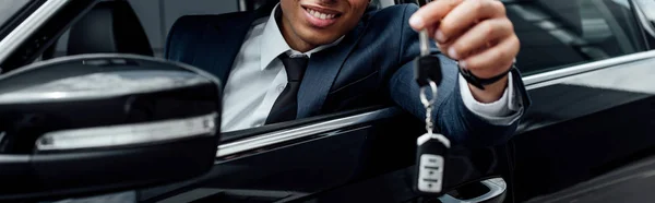 Обрізаний вид усміхненого афроамериканського бізнесмена, що тримає ключ від машини, панорамний постріл — стокове фото